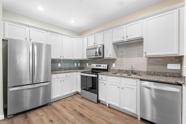 kitchen with appliances with stainless steel finishes, a sink, white cabinets, dark stone countertops, and recessed lighting