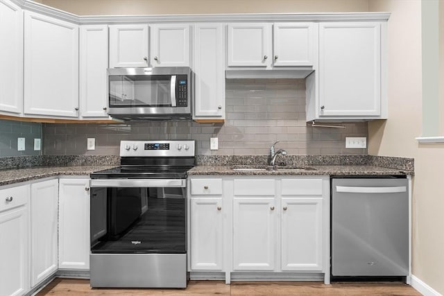 kitchen with appliances with stainless steel finishes, white cabinetry, a sink, tasteful backsplash, and dark stone counters