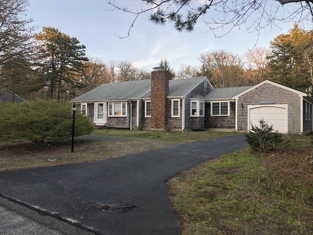ranch-style home featuring a garage, roof with shingles, driveway, and a chimney