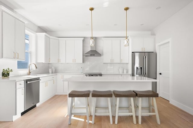 kitchen featuring appliances with stainless steel finishes, a sink, wall chimney exhaust hood, a center island, and light wood finished floors