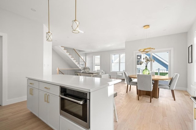 kitchen with oven, light wood-style floors, decorative light fixtures, baseboards, and light countertops