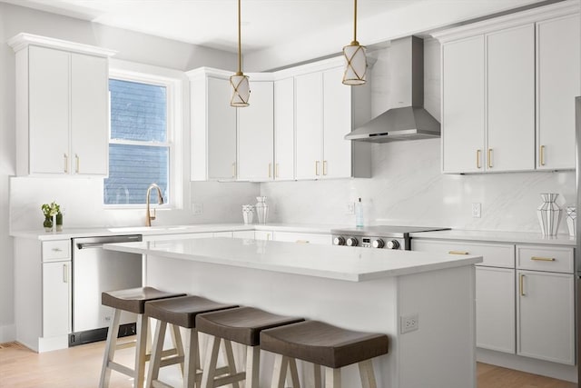 kitchen featuring wall chimney exhaust hood, dishwasher, a breakfast bar, a kitchen island, and light countertops
