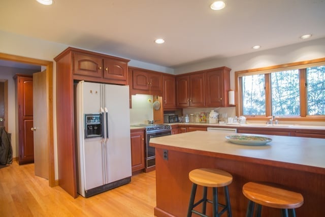 kitchen with white refrigerator with ice dispenser, light hardwood / wood-style floors, a breakfast bar area, and stainless steel range with electric stovetop