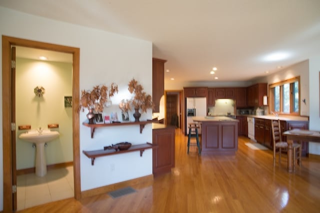 interior space with white appliances, sink, a kitchen island, a breakfast bar, and light wood-type flooring