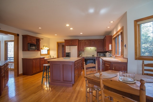 kitchen featuring a center island, light wood-type flooring, white fridge with ice dispenser, built in microwave, and range