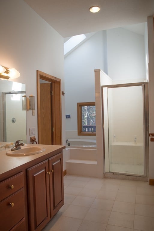 bathroom featuring lofted ceiling with skylight, tile flooring, plus walk in shower, and vanity