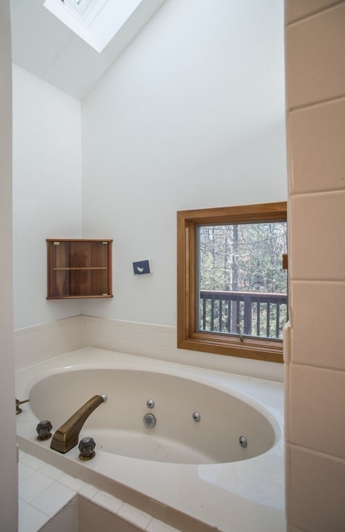 bathroom featuring vaulted ceiling with skylight and tiled bath