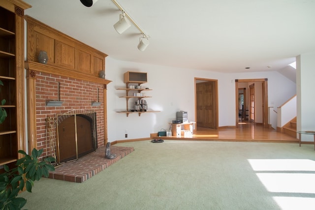 carpeted living room featuring a brick fireplace, brick wall, and rail lighting