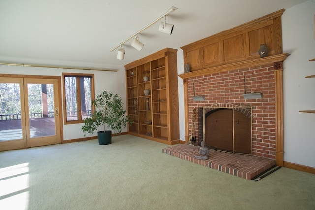 unfurnished living room with light carpet, a brick fireplace, and track lighting