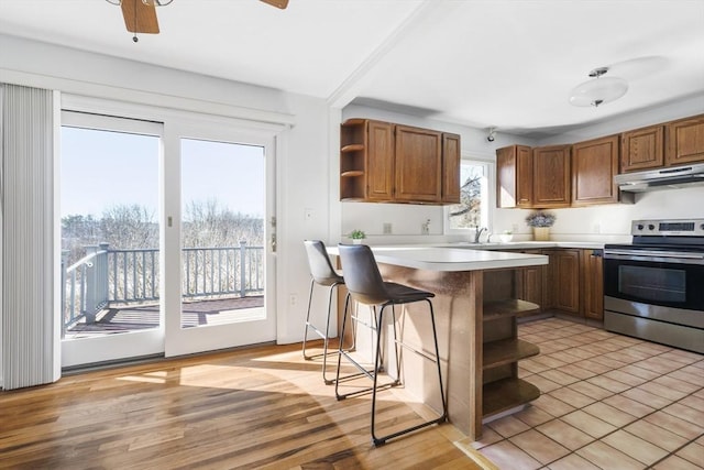 kitchen featuring electric stove, ceiling fan, light hardwood / wood-style floors, a kitchen bar, and kitchen peninsula