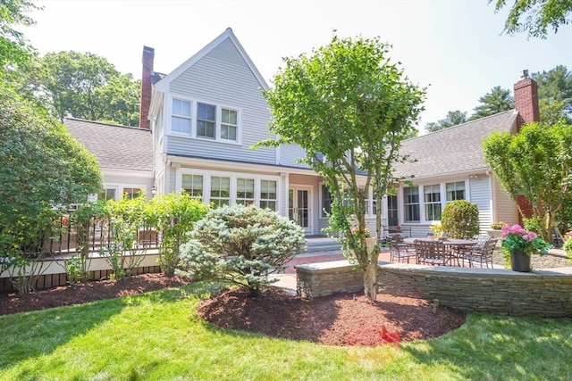 rear view of property featuring a yard, a chimney, a patio, and roof with shingles