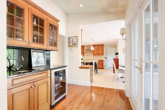 bar featuring backsplash, beverage cooler, light wood-type flooring, wall chimney exhaust hood, and a sink