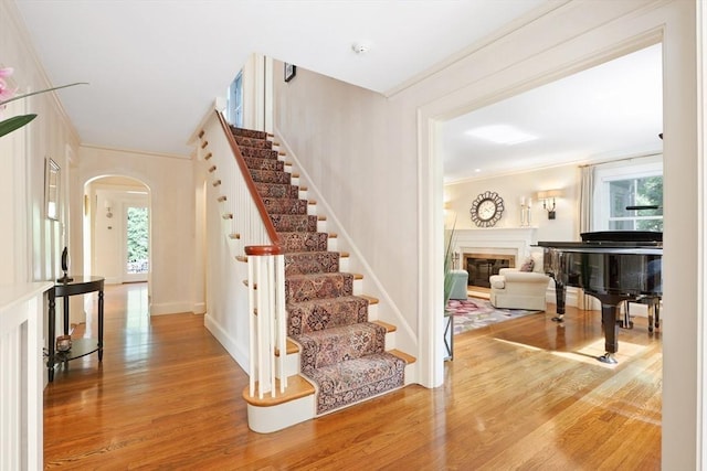 foyer with crown molding, stairway, wood finished floors, arched walkways, and a glass covered fireplace