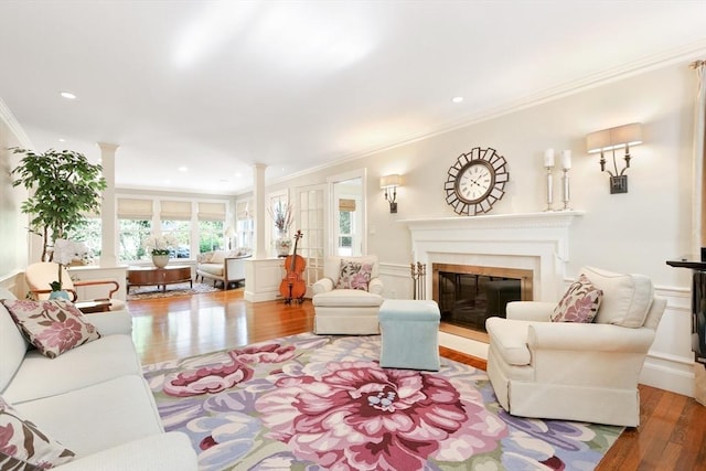 living room featuring wood finished floors, decorative columns, recessed lighting, ornamental molding, and a glass covered fireplace