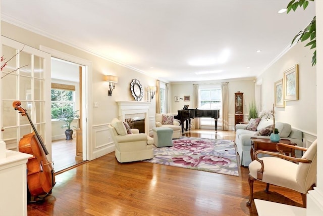 living room featuring a glass covered fireplace, a wainscoted wall, wood finished floors, and crown molding