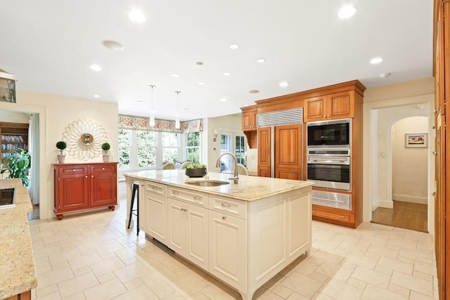 kitchen featuring built in appliances, light stone counters, recessed lighting, arched walkways, and a sink