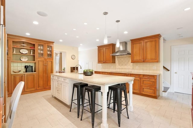 kitchen featuring tasteful backsplash, wall chimney range hood, a large island with sink, a kitchen breakfast bar, and brown cabinetry