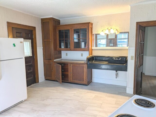 12-14 Essex St, Dover, NH 03820 - kitchen with freestanding refrigerator, glass insert cabinets, wainscoting, brown cabinetry, and a textured ceiling