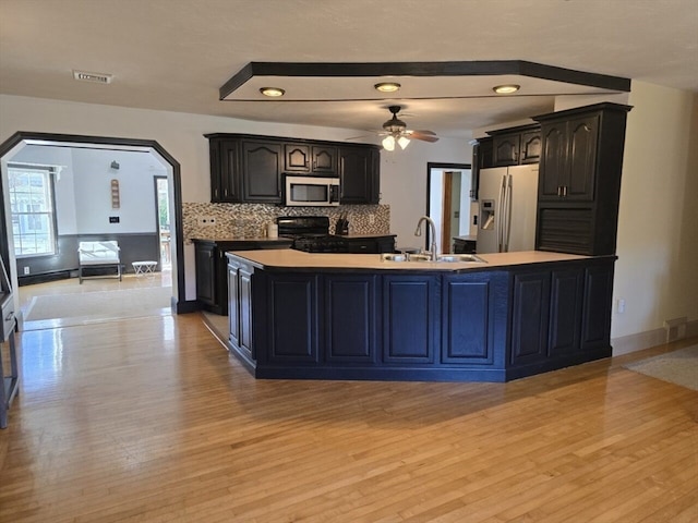 kitchen with stainless steel appliances, light wood-type flooring, backsplash, sink, and ceiling fan