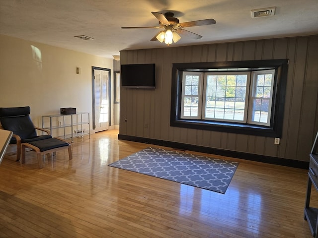 interior space with light wood-type flooring, wood walls, and ceiling fan