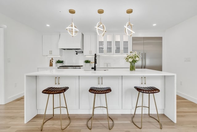 kitchen featuring pendant lighting, custom exhaust hood, light hardwood / wood-style floors, and a kitchen island with sink