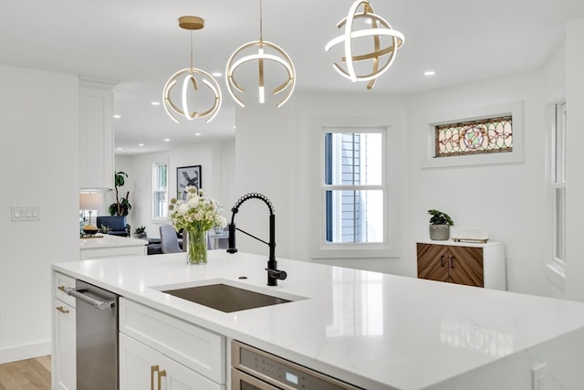 kitchen with white cabinets, hanging light fixtures, a kitchen island with sink, and sink