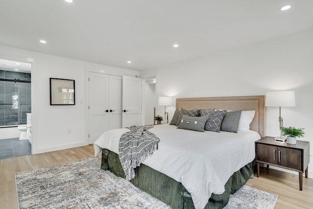 bedroom with light hardwood / wood-style flooring, ensuite bath, and a barn door