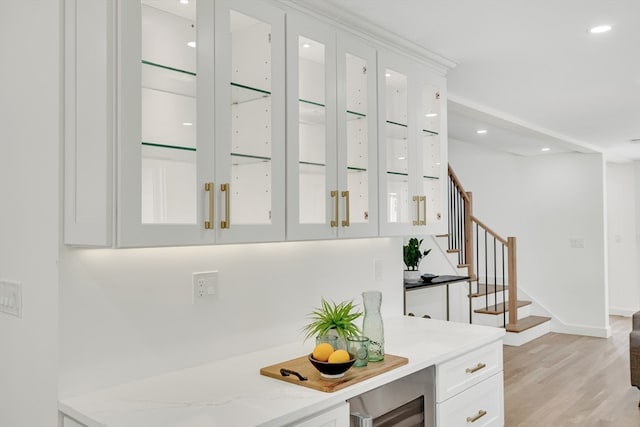 bar with beverage cooler, light stone counters, light hardwood / wood-style floors, and white cabinetry