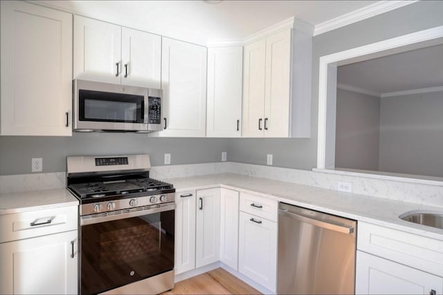 kitchen featuring light stone countertops, white cabinets, light wood-style floors, appliances with stainless steel finishes, and crown molding