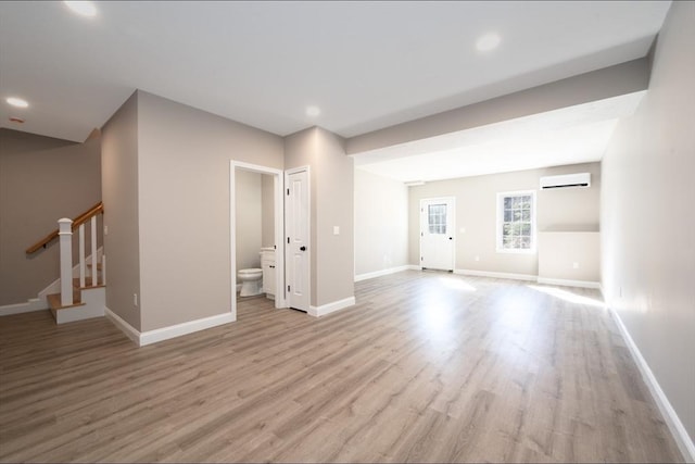 unfurnished living room featuring stairway, wood finished floors, baseboards, recessed lighting, and an AC wall unit