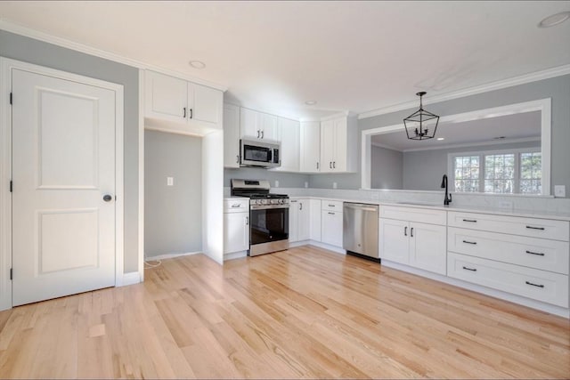 kitchen featuring ornamental molding, a sink, light countertops, appliances with stainless steel finishes, and white cabinetry