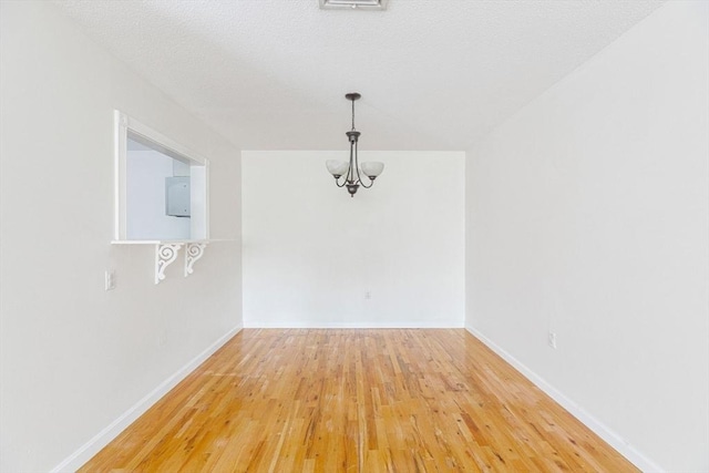 empty room featuring hardwood / wood-style floors, a textured ceiling, and an inviting chandelier