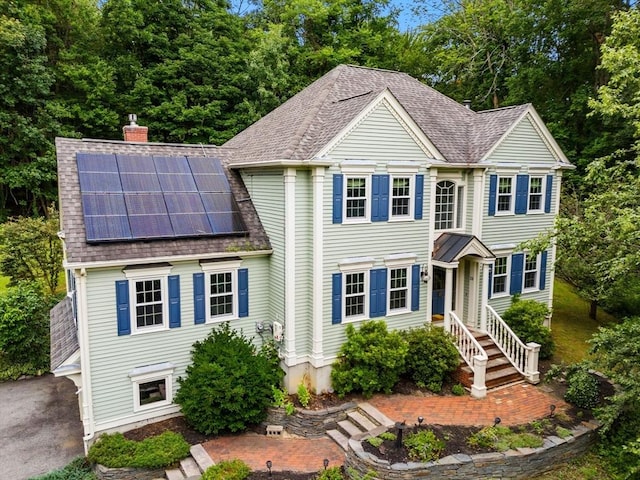 view of front of home featuring solar panels, roof with shingles, and a chimney