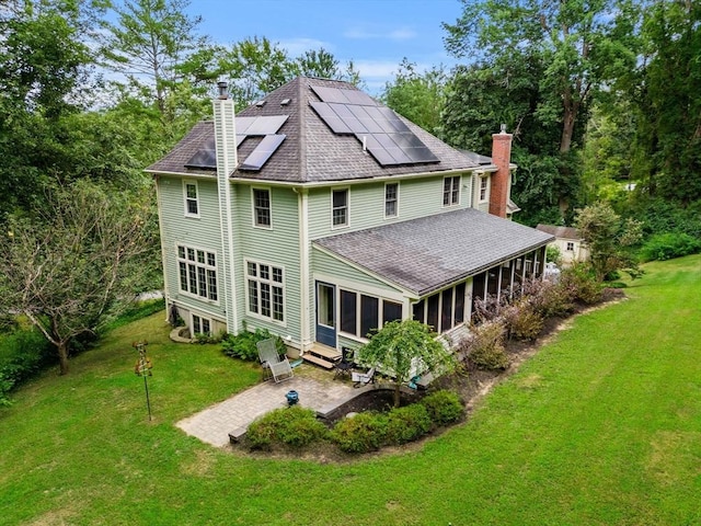 rear view of property with a patio, solar panels, a sunroom, a lawn, and a chimney