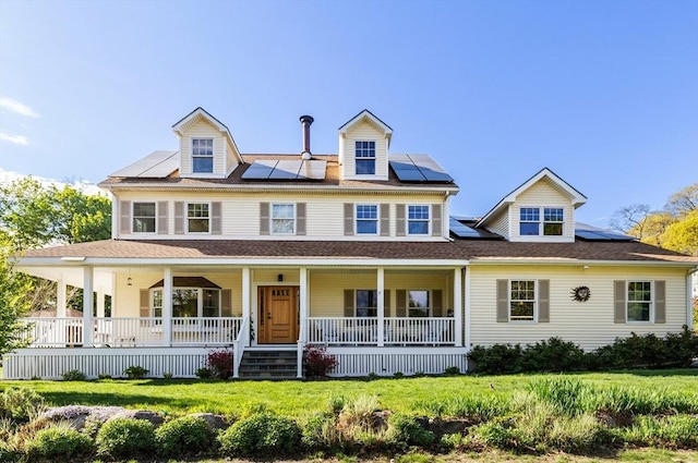view of front of home with a porch, roof mounted solar panels, and a front yard