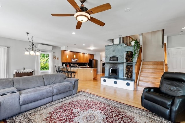 living room with a wall unit AC, light wood finished floors, ceiling fan, stairs, and recessed lighting