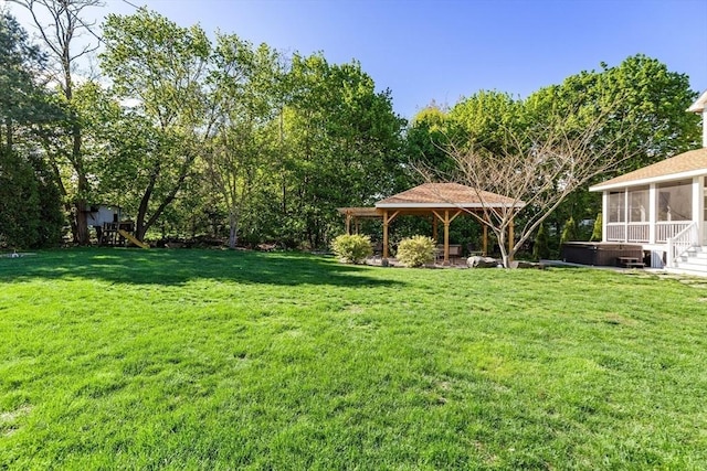 view of grassy yard featuring a hot tub, a sunroom, and a gazebo