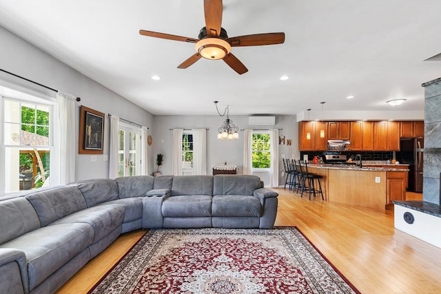 living area with light wood-type flooring, a wall mounted air conditioner, healthy amount of natural light, recessed lighting, and ceiling fan