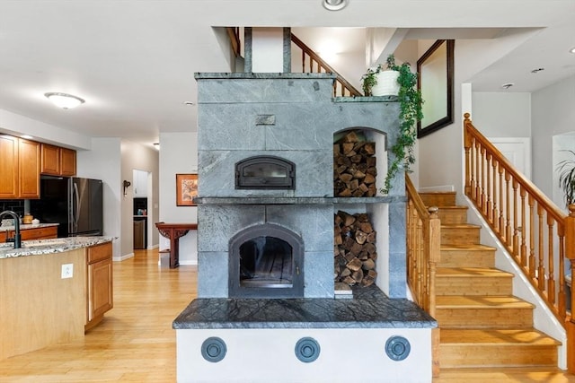 unfurnished living room featuring light wood-type flooring, a tile fireplace, stairway, a sink, and baseboards