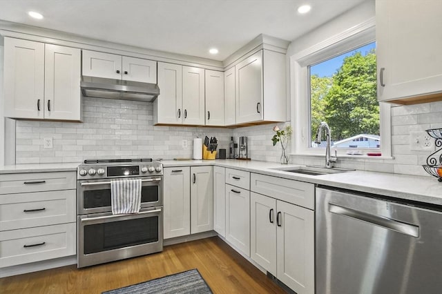 kitchen with appliances with stainless steel finishes, a sink, under cabinet range hood, light countertops, and dark wood finished floors