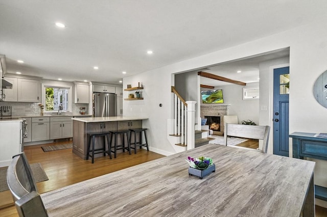 dining room with wood finished floors, recessed lighting, a warm lit fireplace, baseboards, and stairs