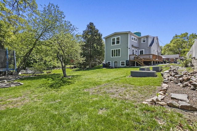 view of grassy yard featuring a trampoline and a wooden deck