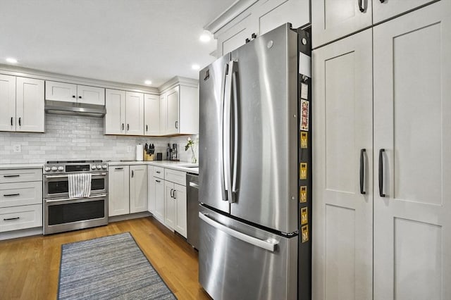 kitchen featuring stainless steel appliances, under cabinet range hood, light countertops, backsplash, and white cabinetry