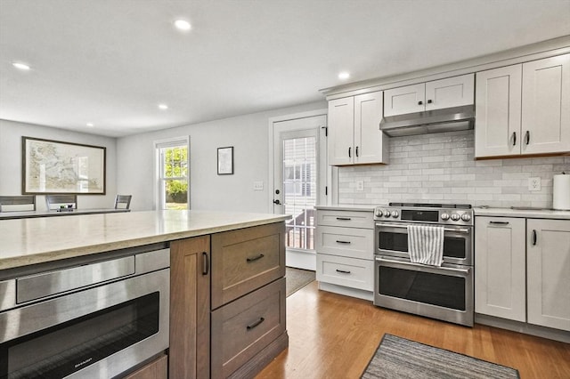 kitchen featuring appliances with stainless steel finishes, under cabinet range hood, recessed lighting, tasteful backsplash, and light wood-style flooring
