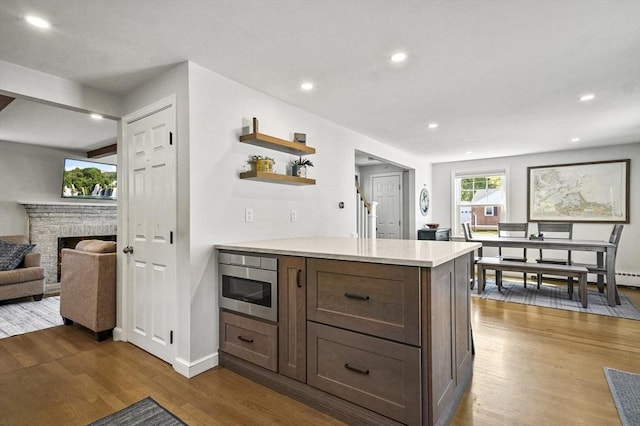 kitchen featuring light countertops, wood finished floors, built in microwave, open shelves, and a peninsula