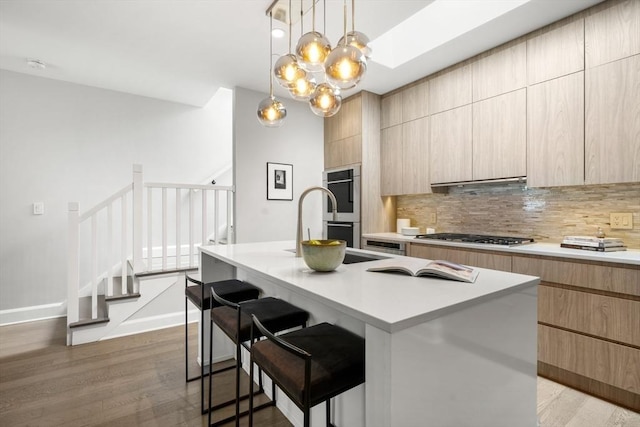 kitchen featuring stainless steel gas cooktop, light wood-style floors, double oven, modern cabinets, and tasteful backsplash