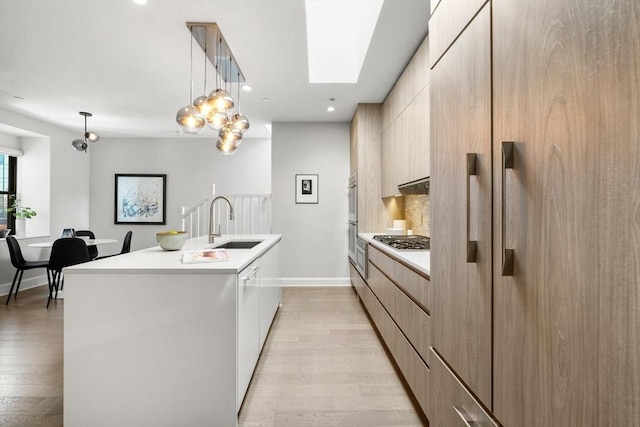 kitchen featuring a sink, light countertops, appliances with stainless steel finishes, modern cabinets, and a kitchen island with sink