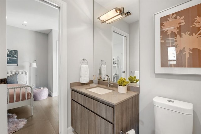 ensuite bathroom featuring toilet, ensuite bath, wood finished floors, baseboards, and vanity