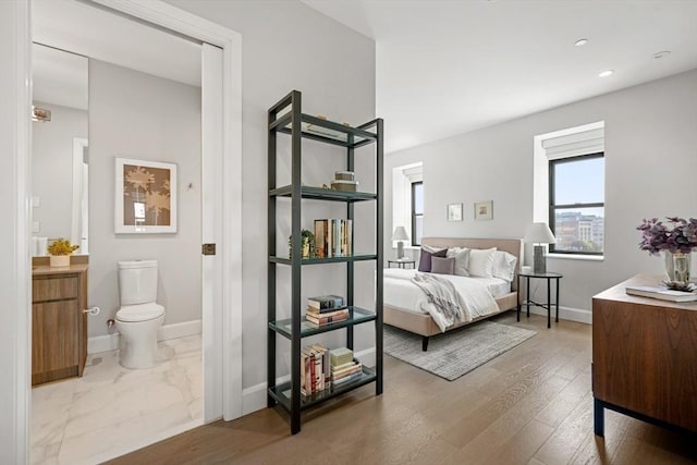 bedroom featuring wood finished floors, baseboards, ensuite bath, and recessed lighting