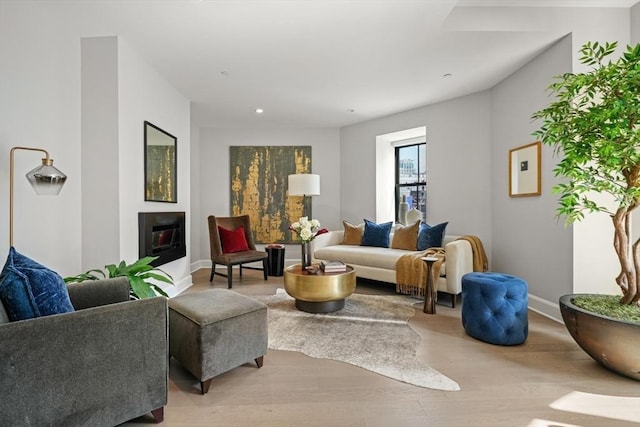 living room with light wood finished floors, a glass covered fireplace, and baseboards